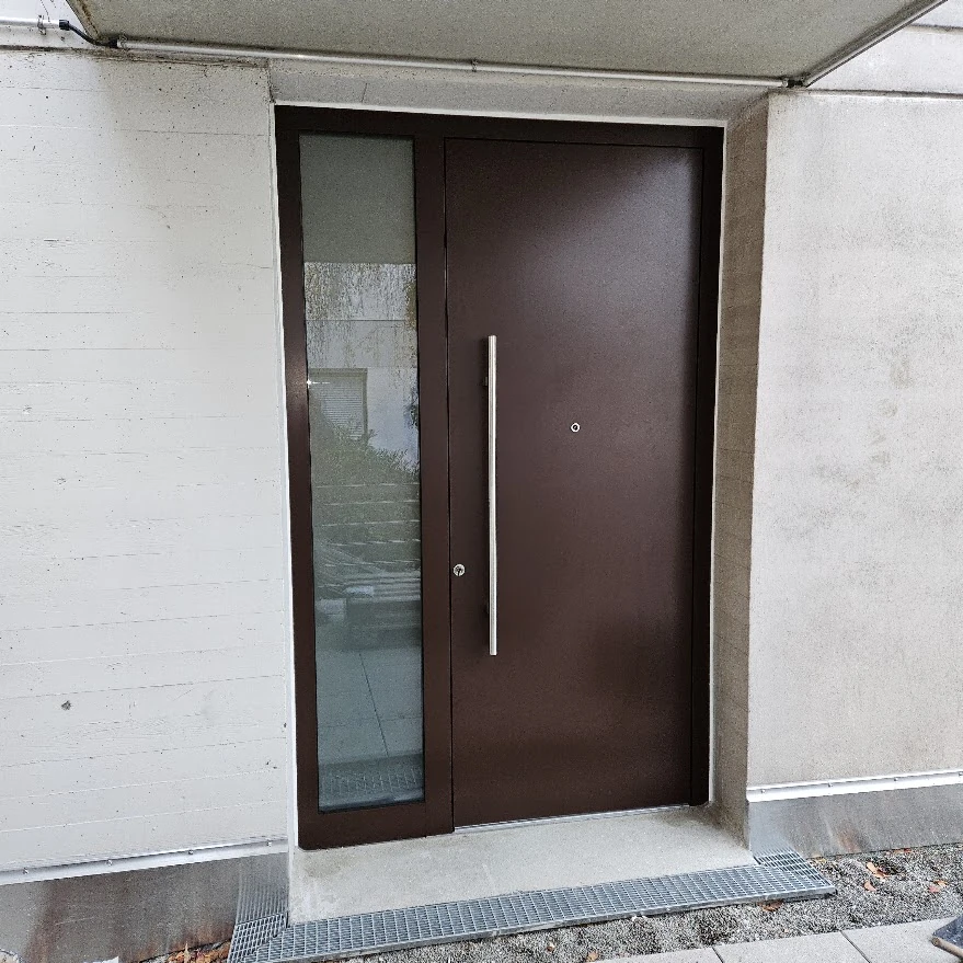 Schokoladenbraune Aluminium-Haustür in RAL 8017 mit glattem Türblatt, Edelstahl-Stangengriff und hohem Klarglas-Seitenteil