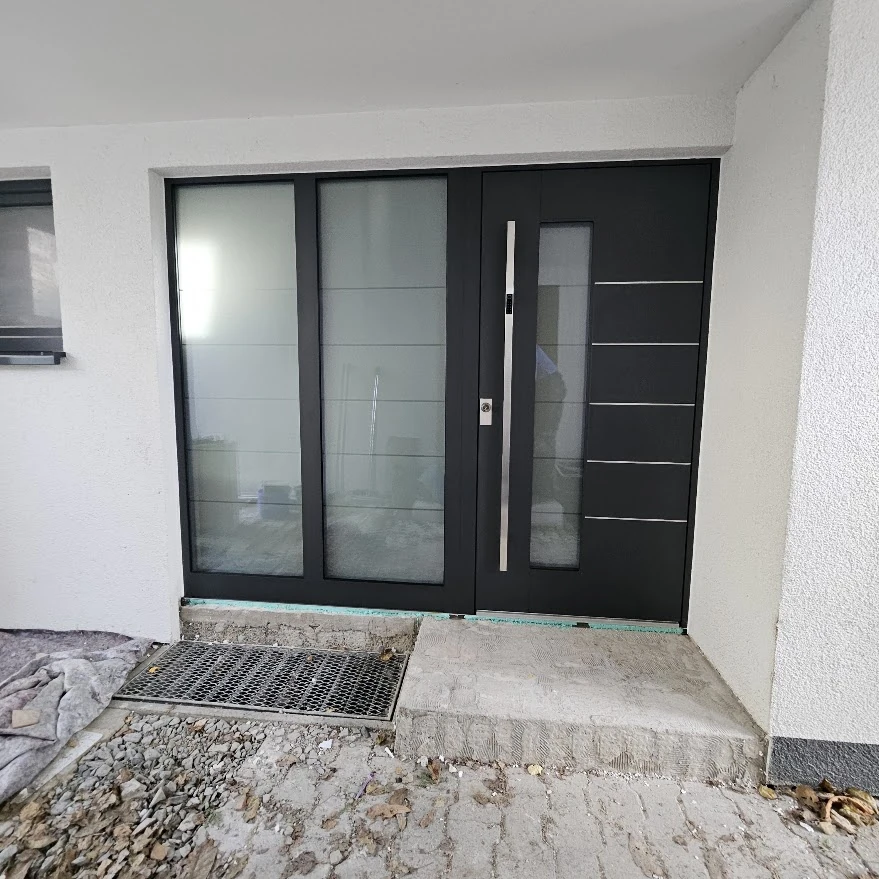 Anthrazitfarbene Inotherm Haustür in RAL 7016 mit zweiteiligem Glas-Seitenteil links und Edelstahlgriff mit Codetastatur im Neubau
