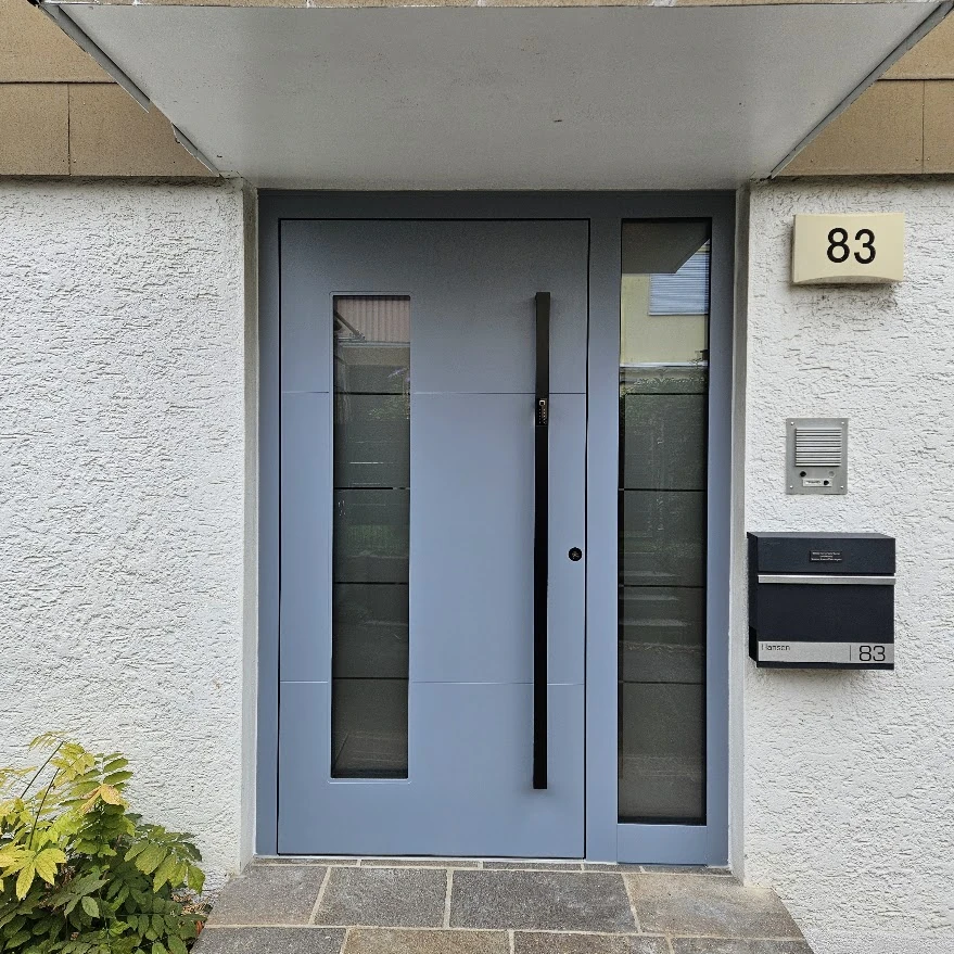 Inotherm Haustür in RAL 5014 Taubenblau mit rechtem Glas-Seitenteil und schwarzem Inosmart-Griff unter einem Vordach